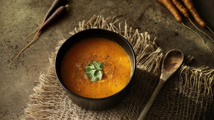 A bowl of carrot soup on a burlap cloth with a wooden spoon