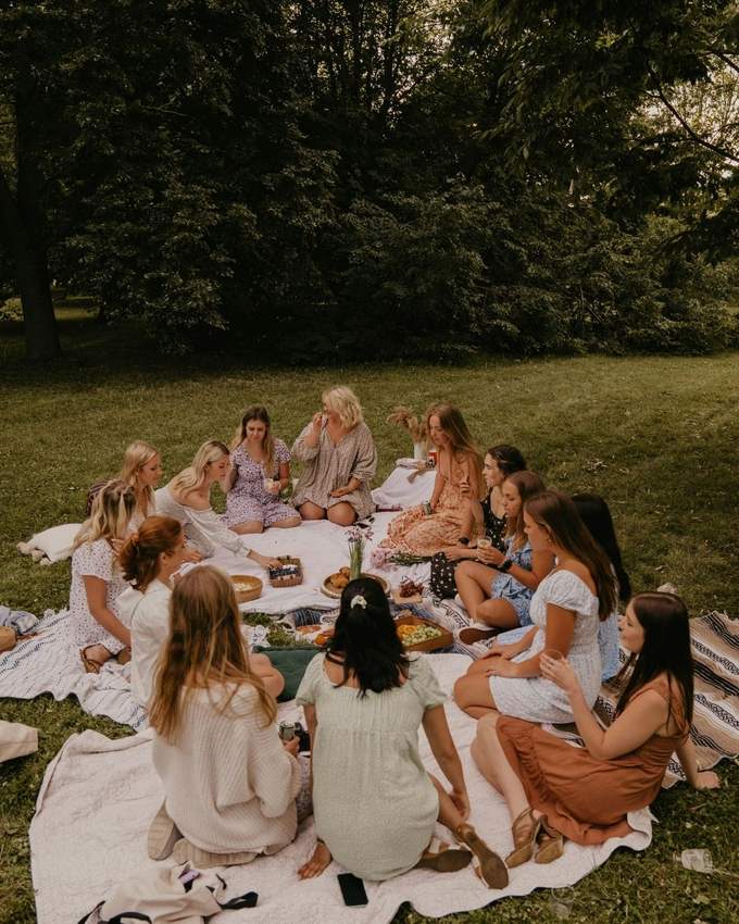 A circle of women sharing a picnic on blankets under big trees